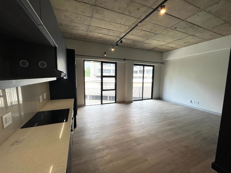 Modern open-plan living area featuring an exposed concrete ceiling, sleek kitchen with quartz countertops, and large sliding doors leading to a balcony.