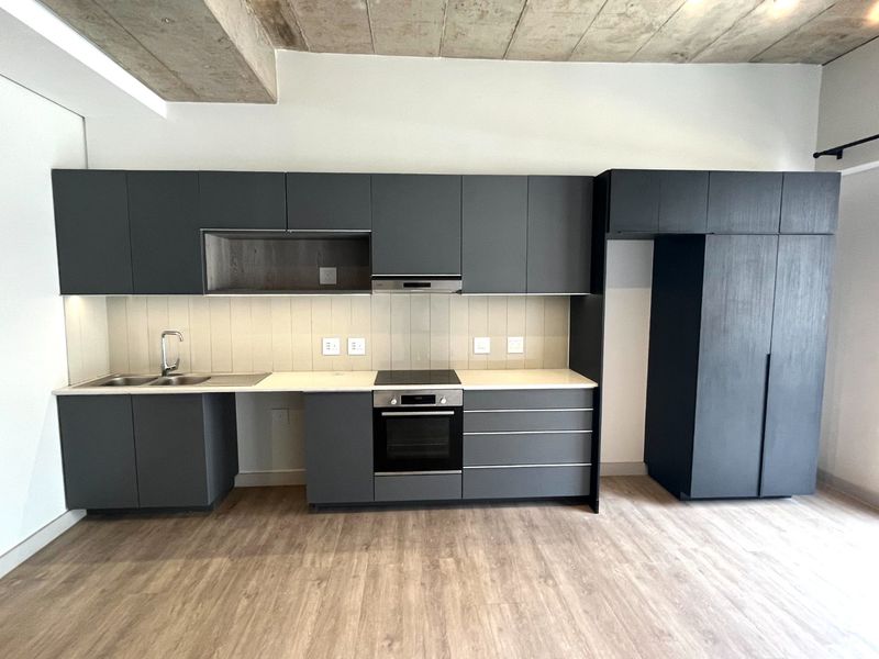 Modern kitchen featuring dark grey cabinetry, stone countertops, integrated oven and hob, and an exposed concrete ceiling in an open-plan layout.