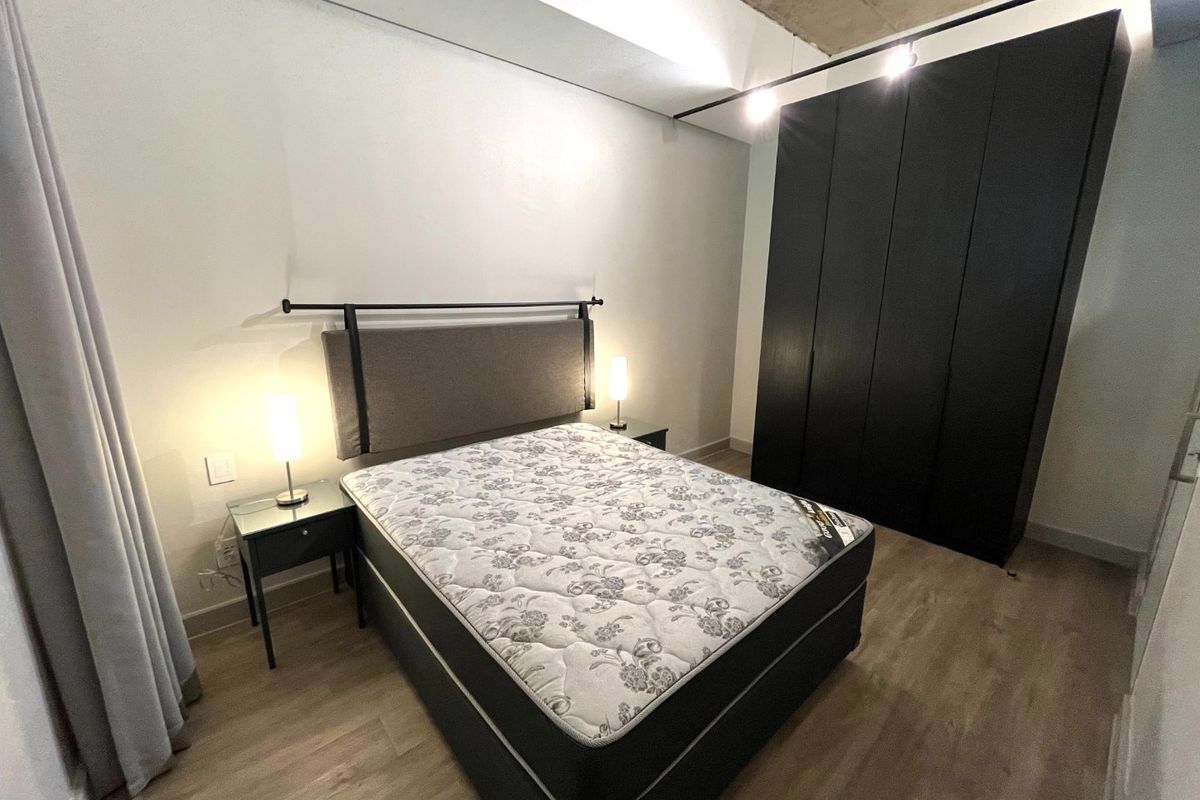 Modern bedroom featuring a high-ceiling design with exposed concrete, integrated black cabinetry, and light wood-look flooring.