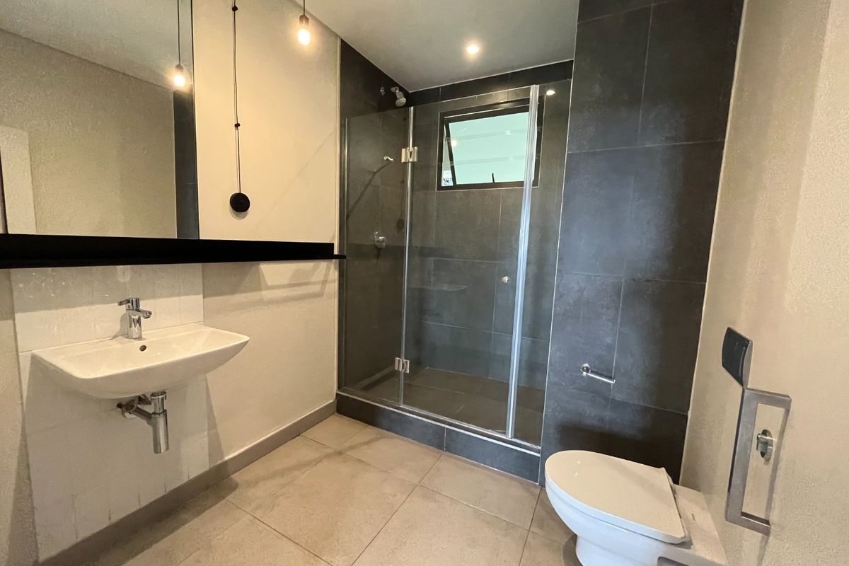 Modern bathroom featuring a wall-mounted basin, a glass-enclosed walk-in shower with dark tiling, and a wall-hung toilet.
