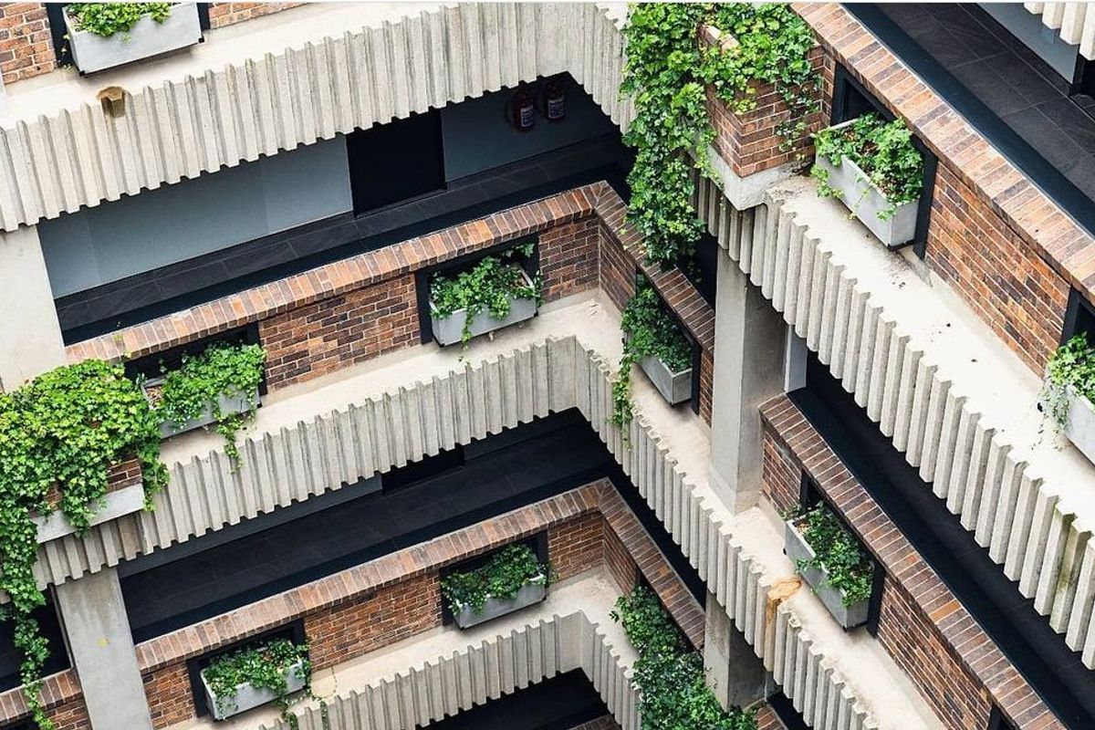 An elevated view of an apartment building's central atrium, featuring tiered brick and concrete balconies with integrated planter boxes.