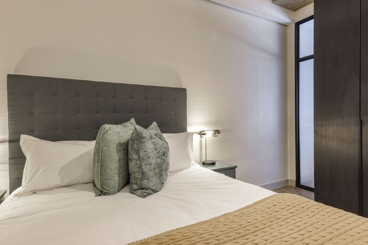 A modern bedroom featuring a built-in wardrobe with a frosted glass door and neutral finishes.