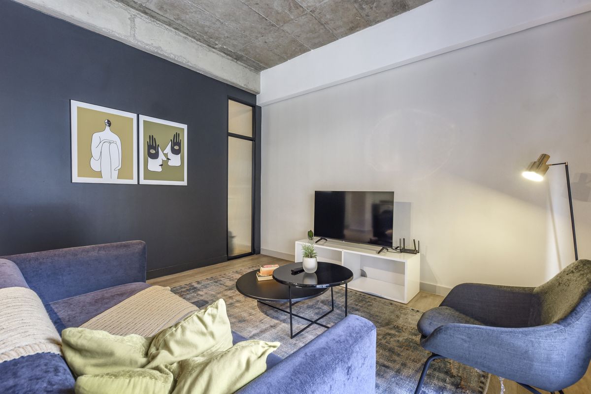 Modern living room featuring an exposed concrete ceiling, a dark accent wall, and a sleek internal glass door, creating a contemporary urban aesthetic.