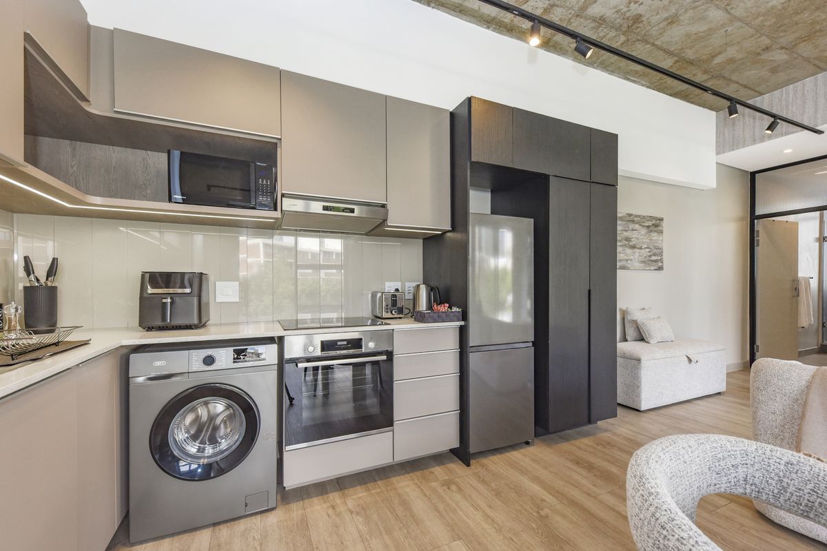 Modern kitchen featuring sleek cabinetry, integrated appliances, glass splashback, and exposed concrete ceiling, seamlessly blending into the open-plan living area.
