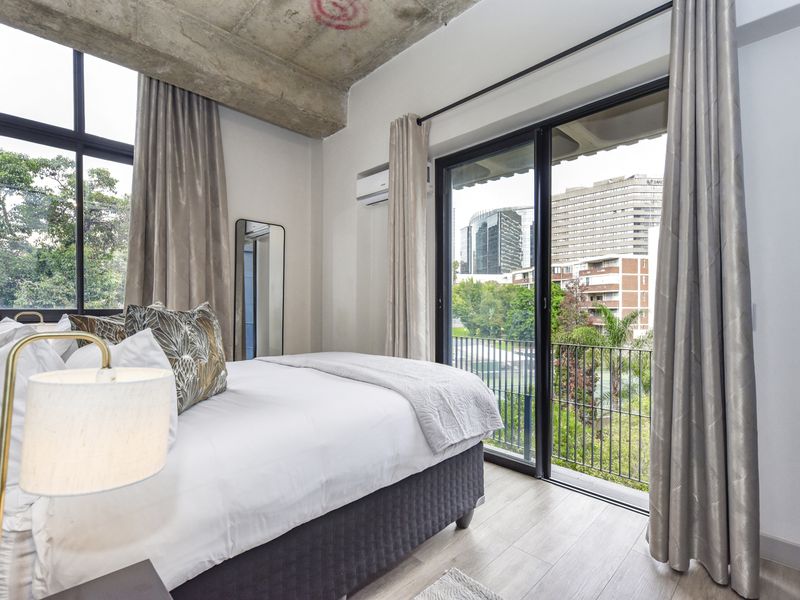 Modern bedroom featuring an exposed concrete ceiling, laminate flooring, and large sliding glass doors opening onto a balcony with urban views.