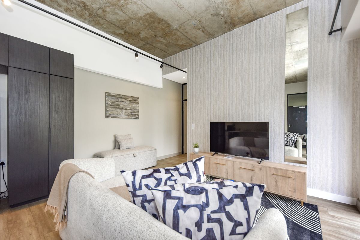 Modern living room featuring an exposed concrete ceiling, track lighting, built-in storage cabinetry, and a full-length wall mirror.