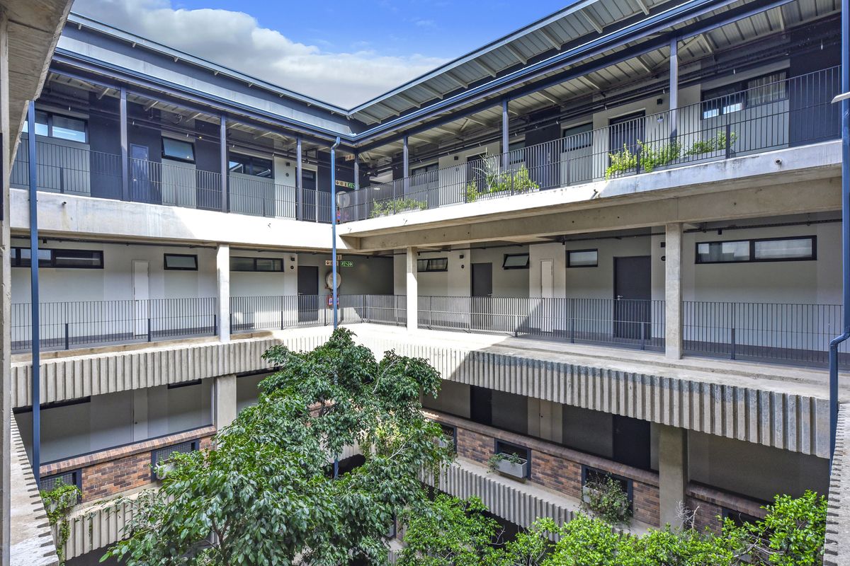 A modern apartment complex featuring a central courtyard with multi-level walkways, metal railings, and exposed concrete architectural elements.