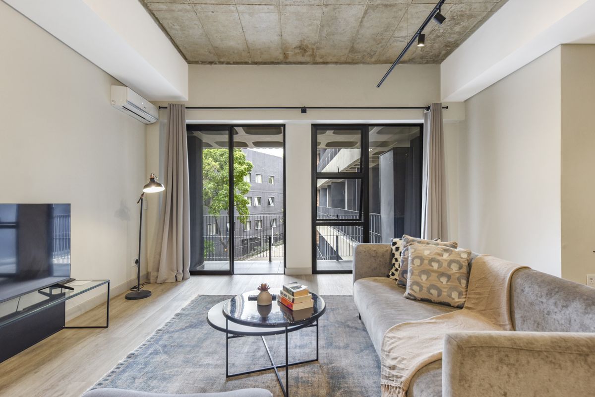 Modern living room featuring an exposed concrete ceiling, track lighting, split-system air conditioning, and large aluminium sliding doors leading to a balcony.