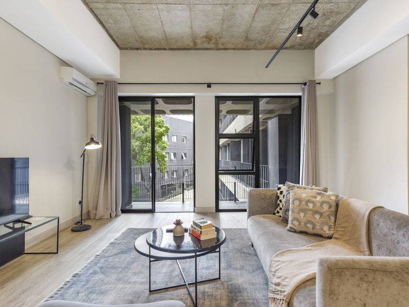 Modern living room featuring an exposed concrete ceiling, track lighting, split-system air conditioning, and large aluminium sliding doors leading to a balcony.