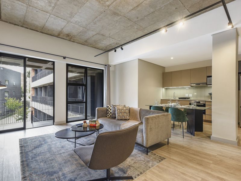 Modern open-plan living area featuring an exposed concrete ceiling, track lighting, and a sleek kitchen with integrated appliances and glass splashback.