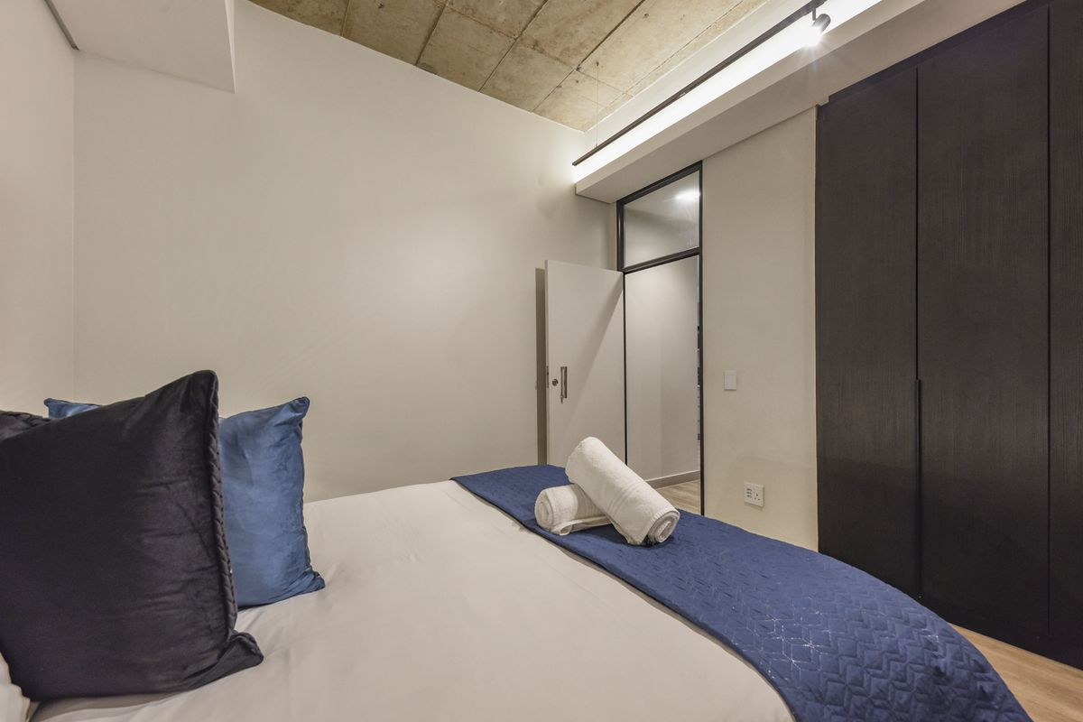 Modern bedroom featuring an exposed concrete ceiling, sleek built-in dark cabinetry, and warm recessed lighting, creating a contemporary and minimalist living space.