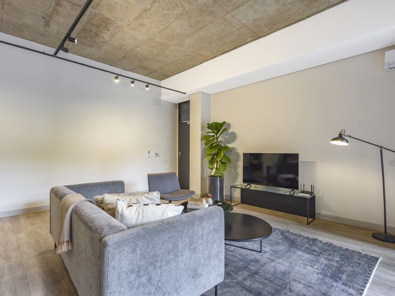 Modern living room featuring an exposed concrete ceiling, track lighting, and split-system air conditioning, finished with contemporary laminate flooring.