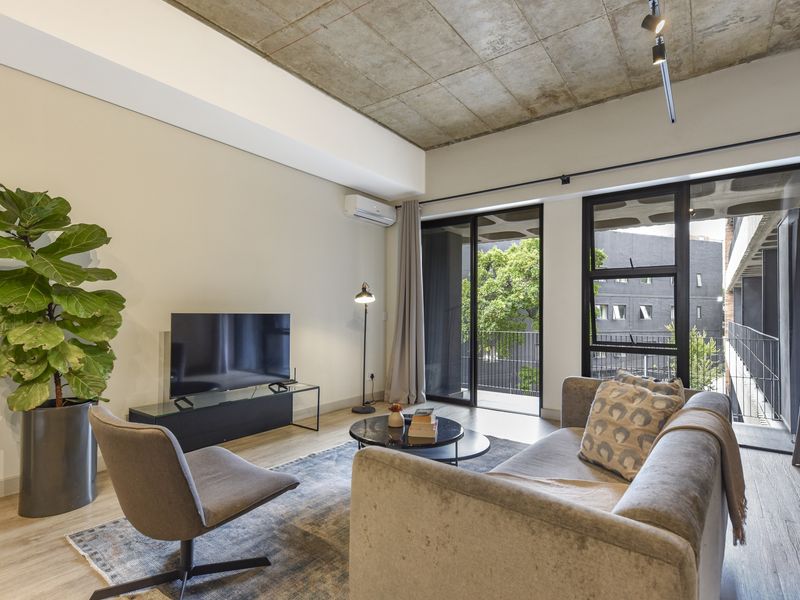 Modern living room featuring an exposed concrete ceiling, track lighting, split-system air conditioning, and large sliding glass doors leading to a balcony.