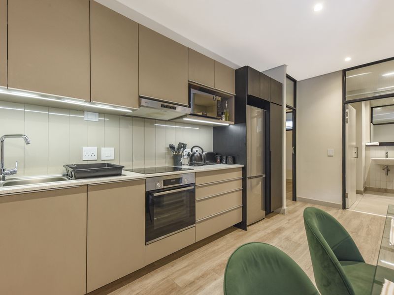 Modern kitchen featuring sleek handleless cabinetry, integrated appliances, electric hob, and a clean, contemporary aesthetic with wood-look flooring.
