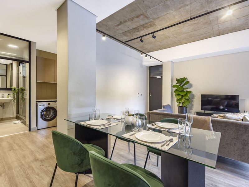 Modern open-plan living and dining area featuring an exposed concrete ceiling, track lighting, and a convenient integrated laundry nook with built-in cabinetry.