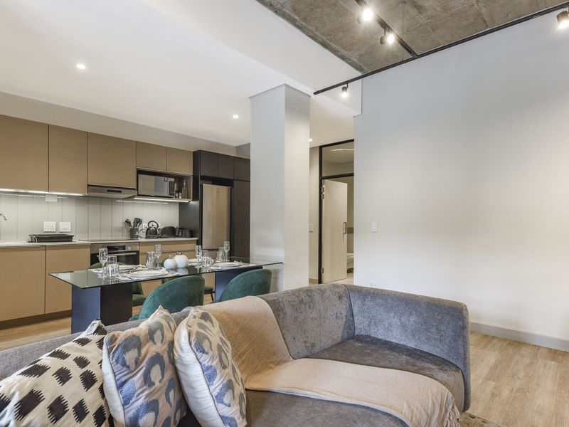 Modern open-plan living area featuring a sleek kitchen with built-in cabinetry, integrated appliances, and an industrial-style exposed concrete ceiling with track lighting.