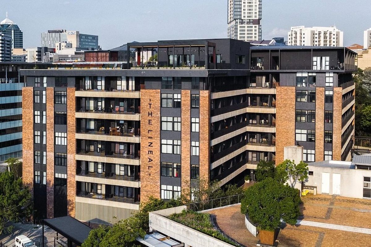 Aerial view of The Lineal apartment complex, showcasing its modern brick and metal facade, private balconies, and rooftop terrace area.