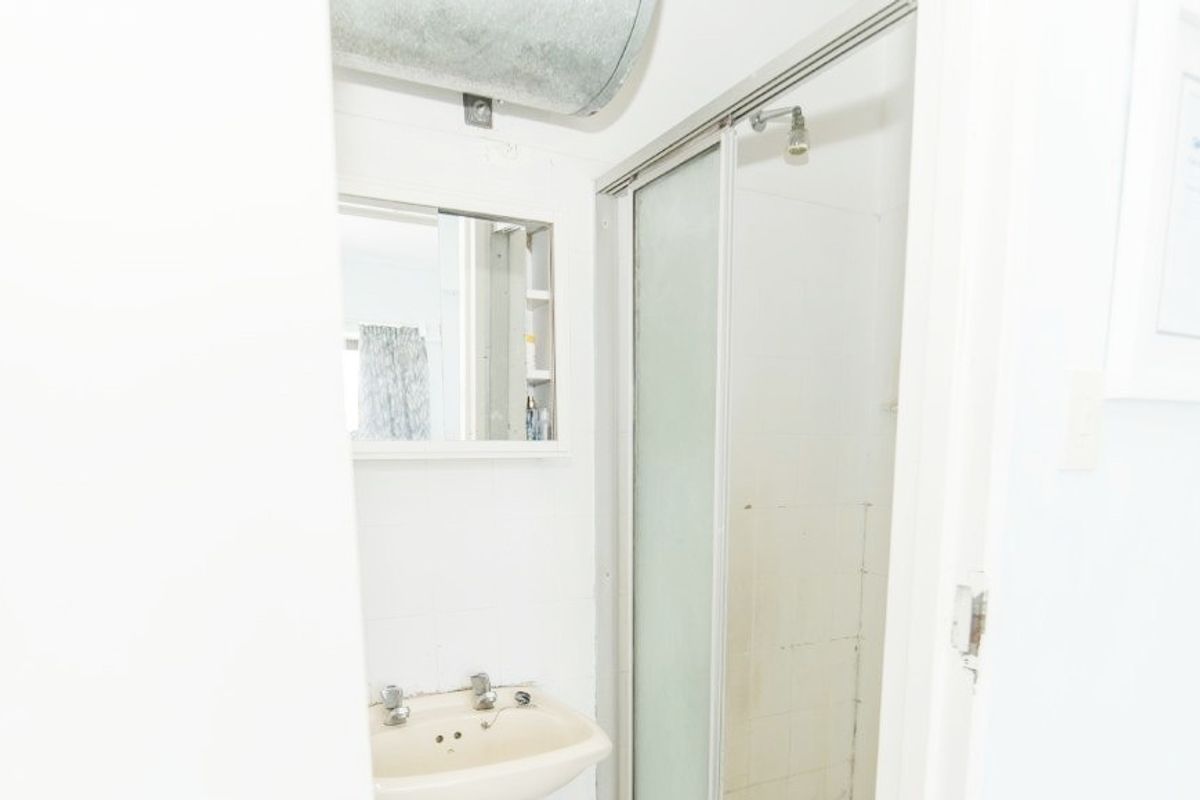 A compact bathroom featuring a shower enclosure, wall-mounted basin, and medicine cabinet, with exposed ducting visible above.