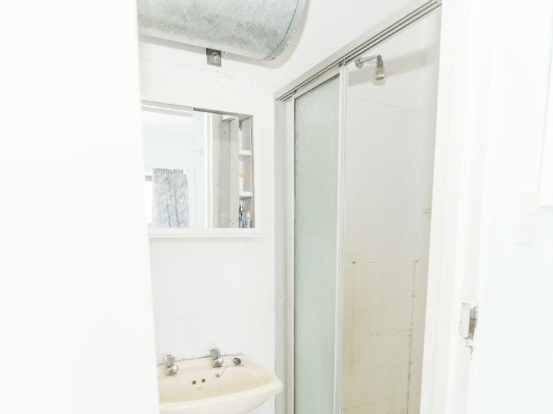 A compact bathroom featuring a shower enclosure, wall-mounted basin, and medicine cabinet, with exposed ducting visible above.