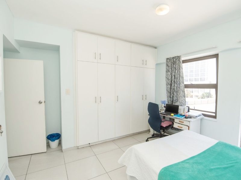 A bedroom featuring built-in cupboards, tiled flooring, and large windows allowing for natural light.