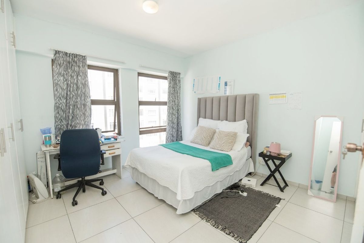 A functional bedroom featuring tiled flooring and built-in cupboards, offering a clean and neutral space with natural light from the windows.