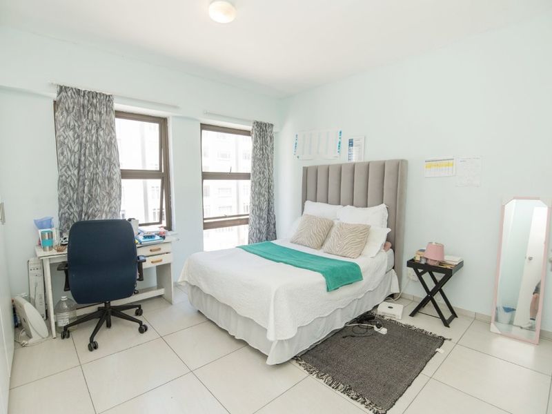 A functional bedroom featuring tiled flooring and built-in cupboards, offering a clean and neutral space with natural light from the windows.