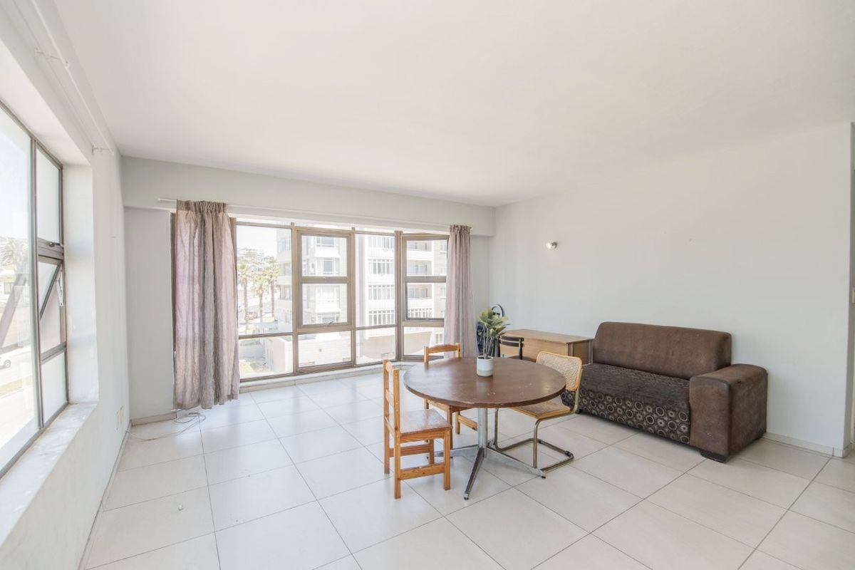 A bright and spacious living area featuring large aluminium-framed windows that provide ample natural light and tiled flooring throughout.