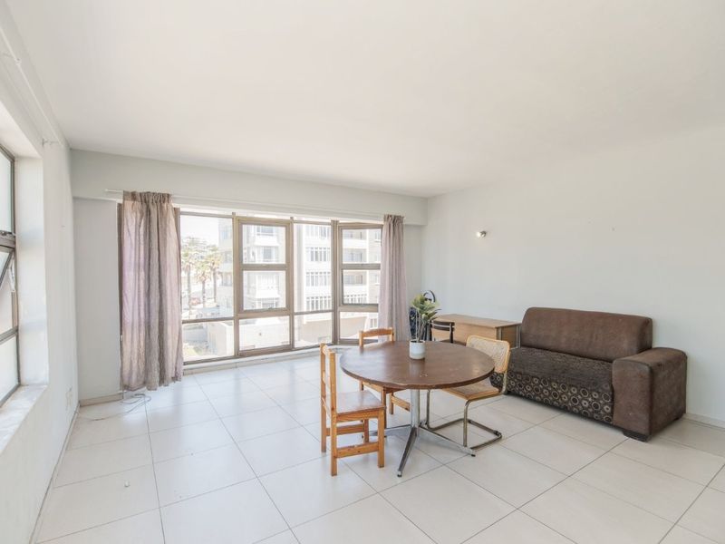 A bright and spacious living area featuring large aluminium-framed windows that provide ample natural light and tiled flooring throughout.
