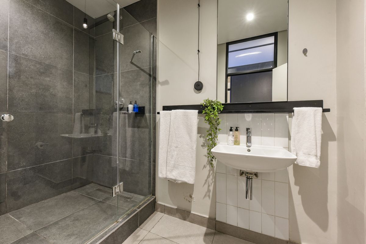 Modern bathroom featuring a spacious walk-in shower with dark grey tiling, a wall-mounted basin, and a large mirror.