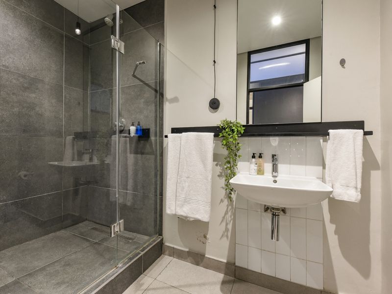 Modern bathroom featuring a spacious walk-in shower with dark grey tiling, a wall-mounted basin, and a large mirror.