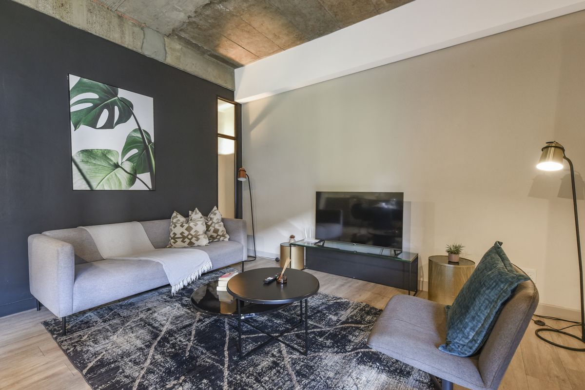 A modern living room featuring an exposed concrete ceiling, laminate flooring, and a striking black accent wall.