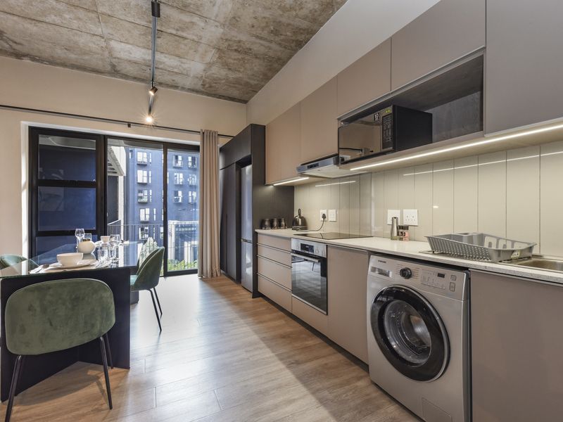 Modern open-plan kitchen and dining area featuring exposed concrete ceilings, sleek cabinetry, integrated appliances, and direct access to a balcony.