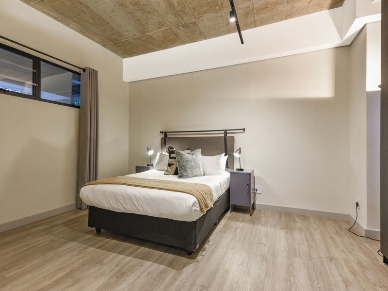 Modern bedroom featuring an exposed concrete ceiling, laminate flooring, track lighting, and a built-in wardrobe.