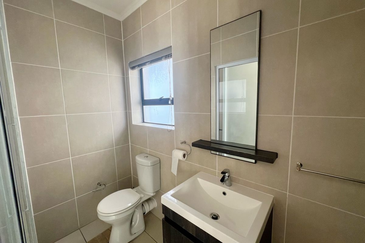 A modern bathroom featuring neutral wall tiles, a vanity with a basin, a wall-mounted mirror, and a toilet.