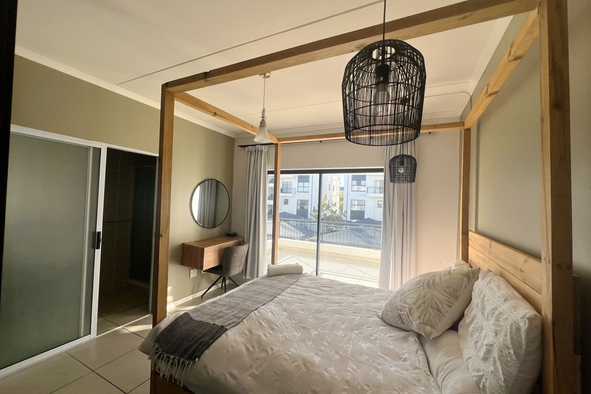 A well-lit bedroom featuring a four-poster bed frame, tiled flooring, and an en-suite bathroom with sliding door access and a private balcony.
