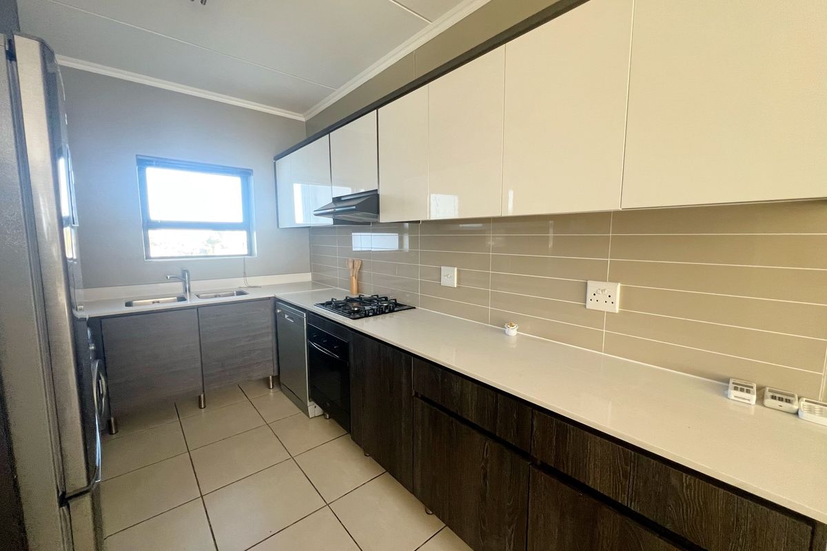 Modern kitchen featuring sleek two-tone cabinetry, stone countertops, a gas hob, built-in oven, extractor fan, and tiled flooring.