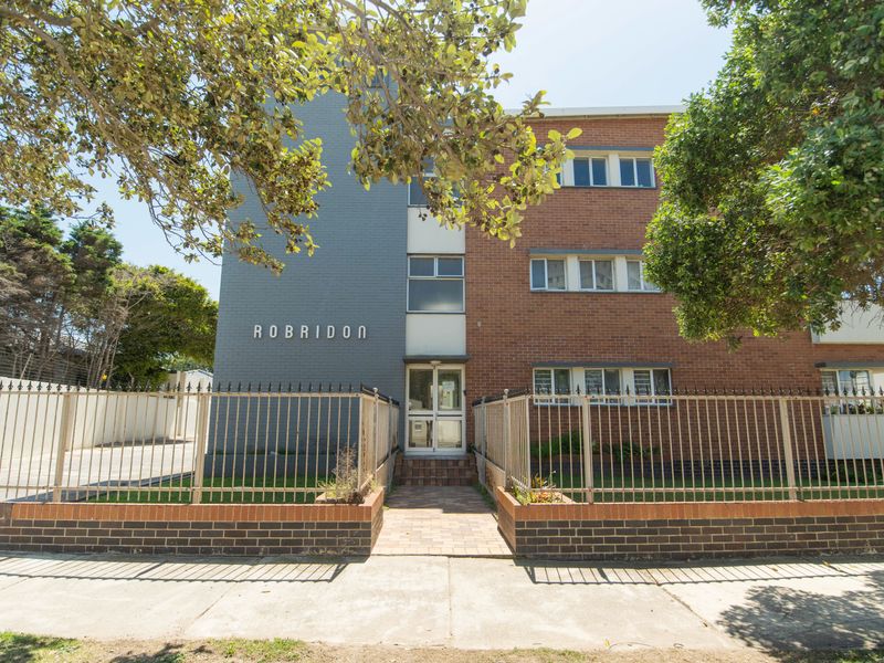 Front elevation of the Robridon apartment complex, featuring a brick and painted facade, secure metal fencing, and a paved pedestrian entrance.
