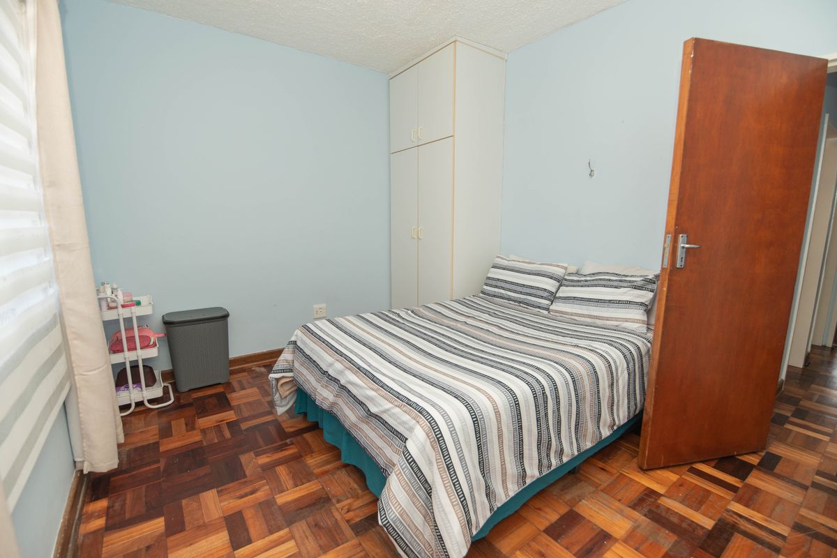A bedroom featuring parquet flooring, a built-in wardrobe, and light blue walls, offering a functional space with classic finishes.