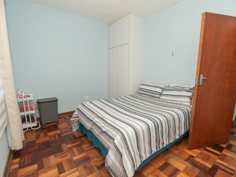 A bedroom featuring parquet flooring, a built-in wardrobe, and light blue walls, offering a functional space with classic finishes.