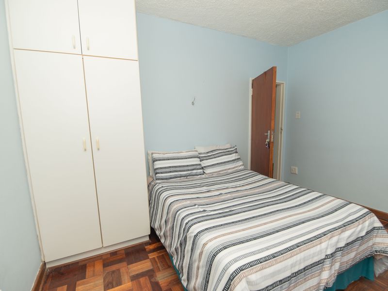 A bedroom featuring built-in cupboards, parquet flooring, and a textured ceiling, offering a functional space with potential for cosmetic updates.