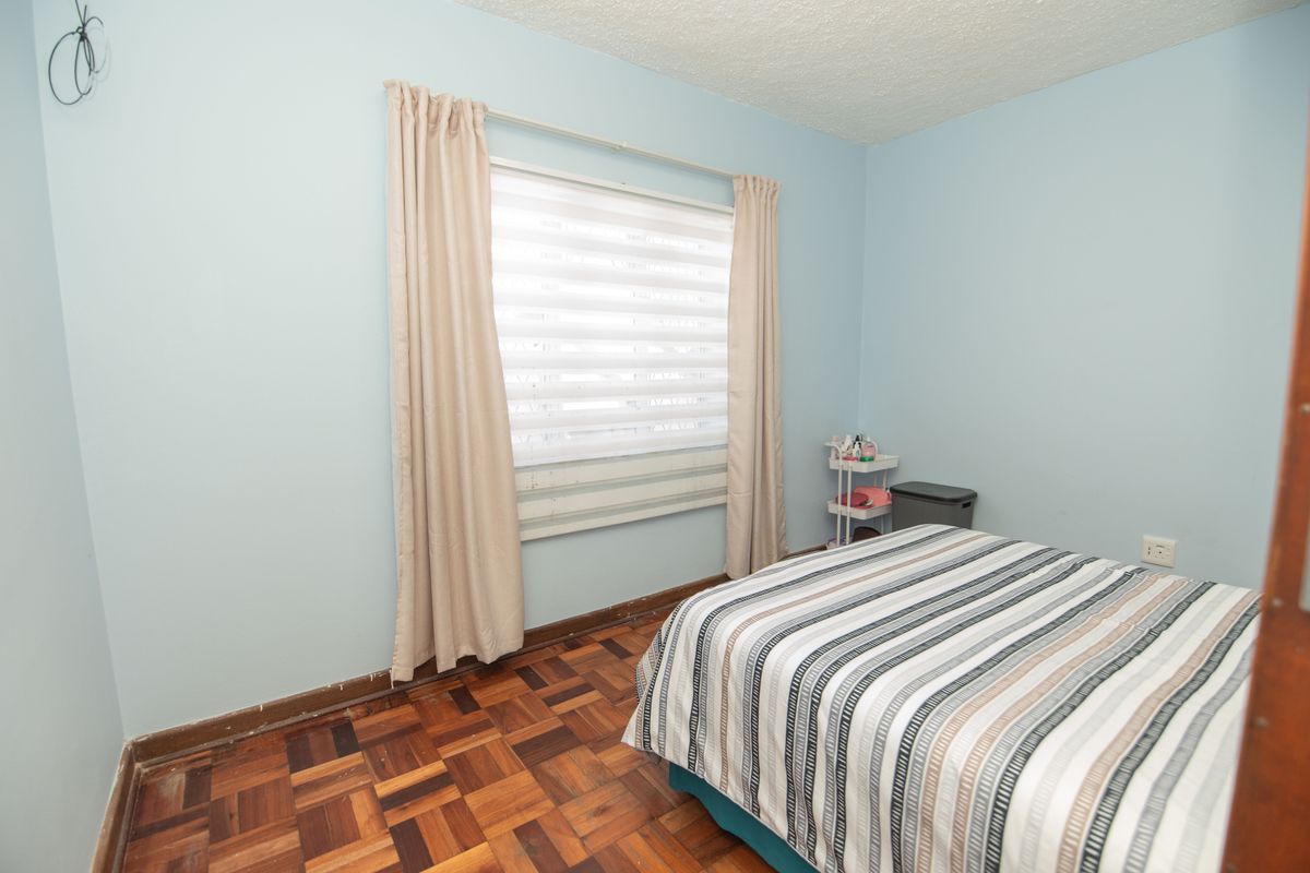 A bedroom featuring parquet flooring, light blue walls, and a window with roller blinds. The room requires minor cosmetic updates and repairs.
