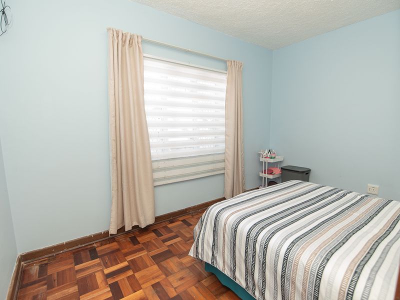 A bedroom featuring parquet flooring, light blue walls, and a window with roller blinds. The room requires minor cosmetic updates and repairs.
