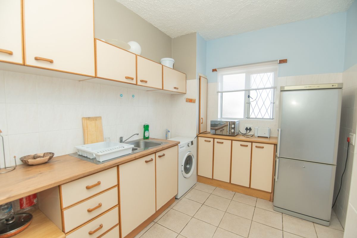 A functional kitchen featuring laminate countertops, ample built-in cabinetry, tiled flooring, and a tiled backsplash with space for a washing machine.