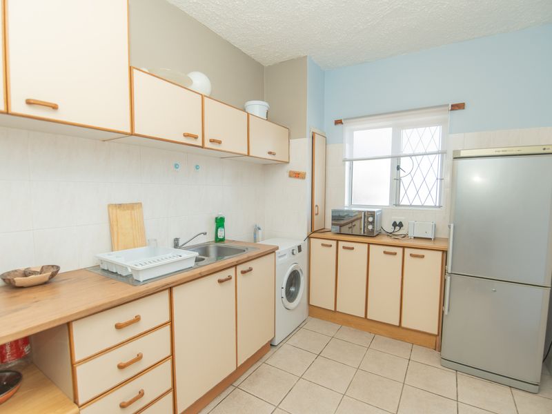 A functional kitchen featuring laminate countertops, ample built-in cabinetry, tiled flooring, and a tiled backsplash with space for a washing machine.