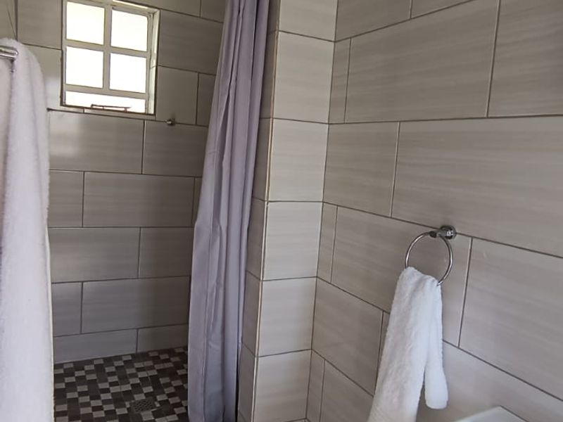A functional bathroom featuring a tiled shower enclosure with a shower head and a pedestal basin.
