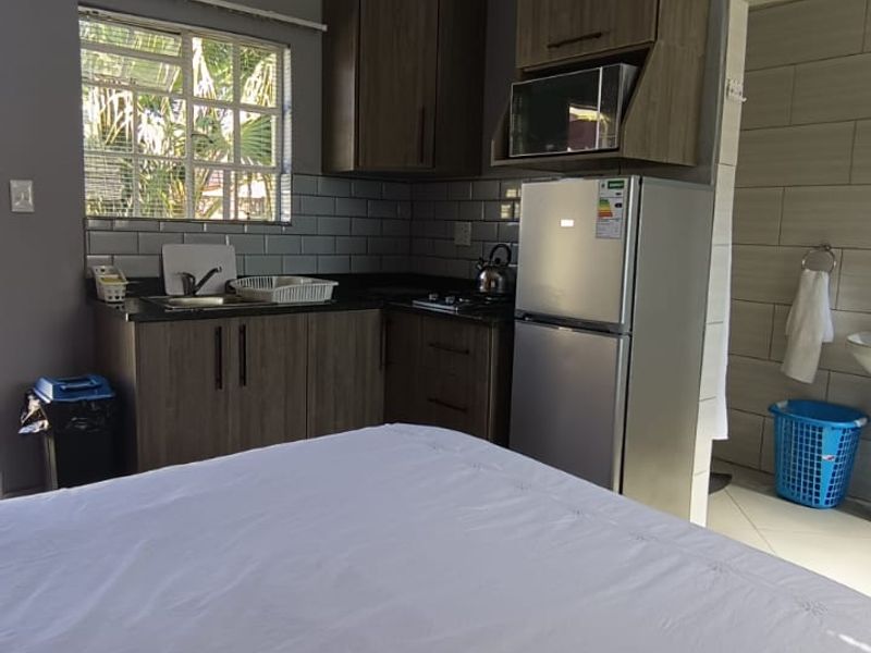 Compact open-plan kitchenette featuring modern wood-finish cabinetry, subway tile backsplash, and integrated appliances, seamlessly connected to the bedroom area.