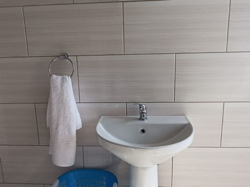 A clean bathroom featuring a white pedestal basin, chrome mixer tap, and neutral ceramic wall and floor tiling.
