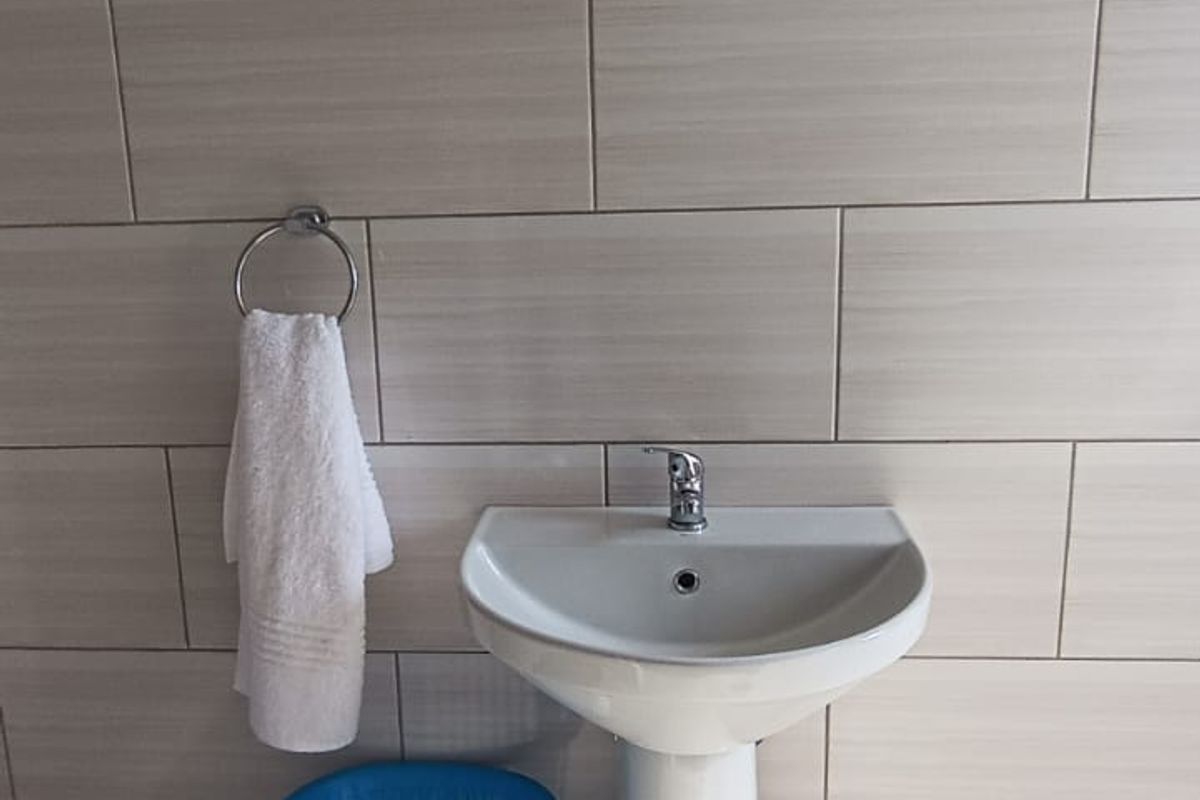 A clean bathroom featuring a white pedestal basin, chrome mixer tap, and neutral ceramic wall and floor tiling.