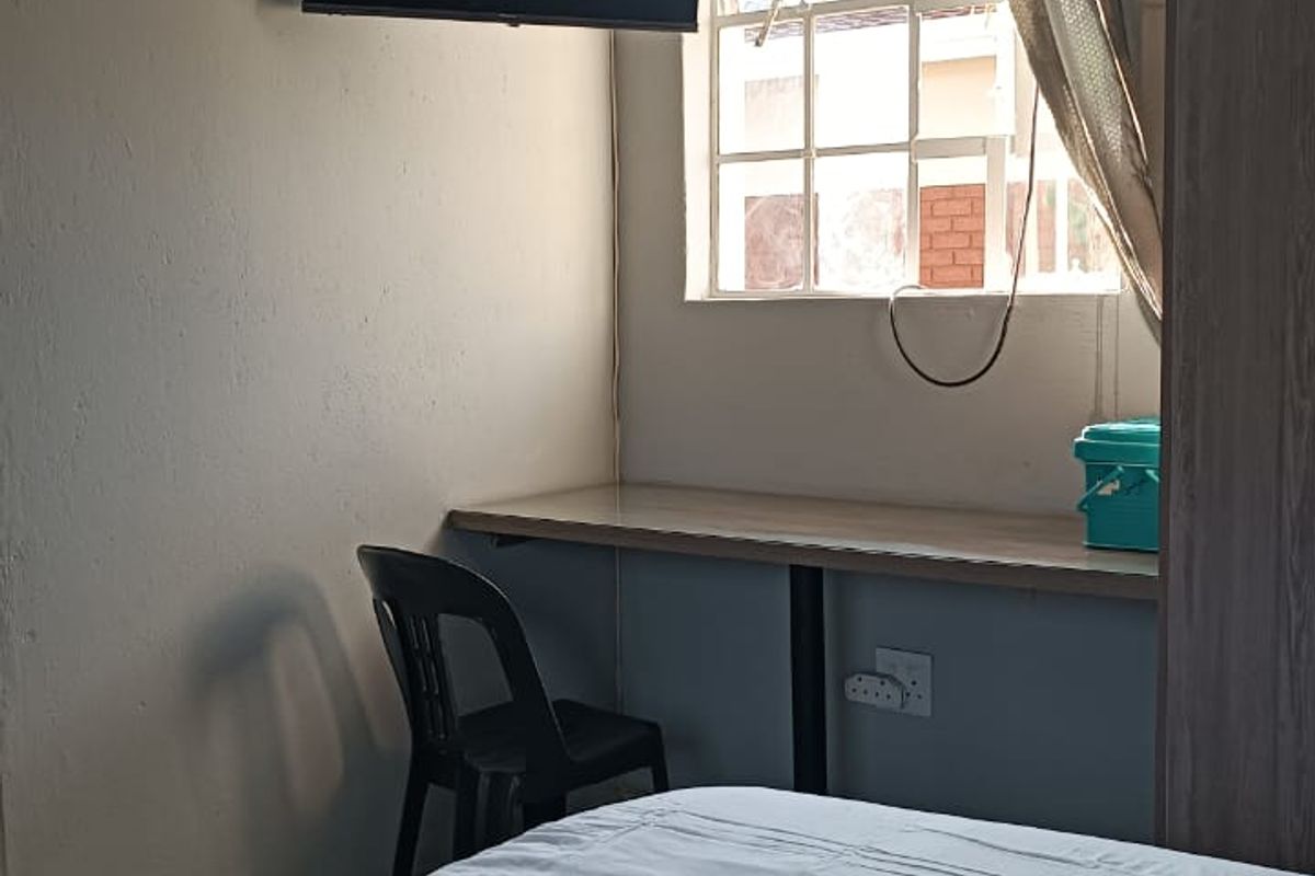 A compact bedroom featuring a built-in desk, wall-mounted television, and a window, providing a functional living space.