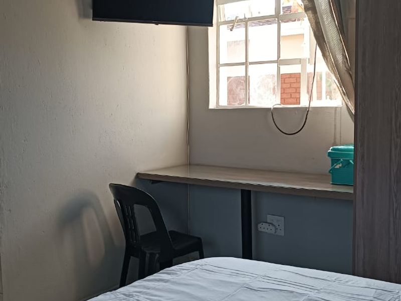 A compact bedroom featuring a built-in desk, wall-mounted television, and a window, providing a functional living space.